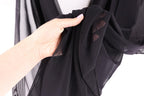 A hand is holding a black fabric with a patterned design, against a white background.