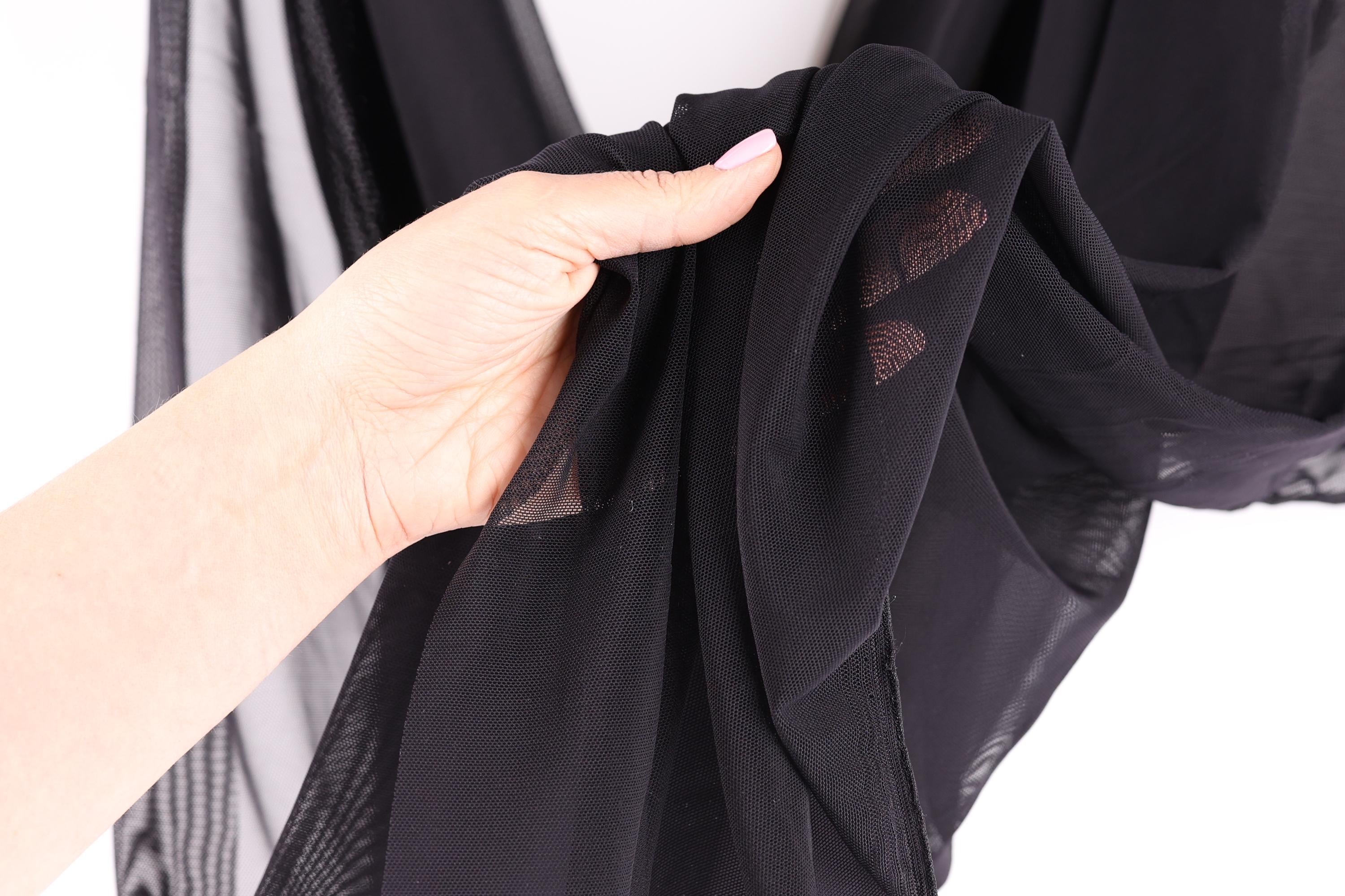 A hand is holding a black fabric with a patterned design, against a white background.