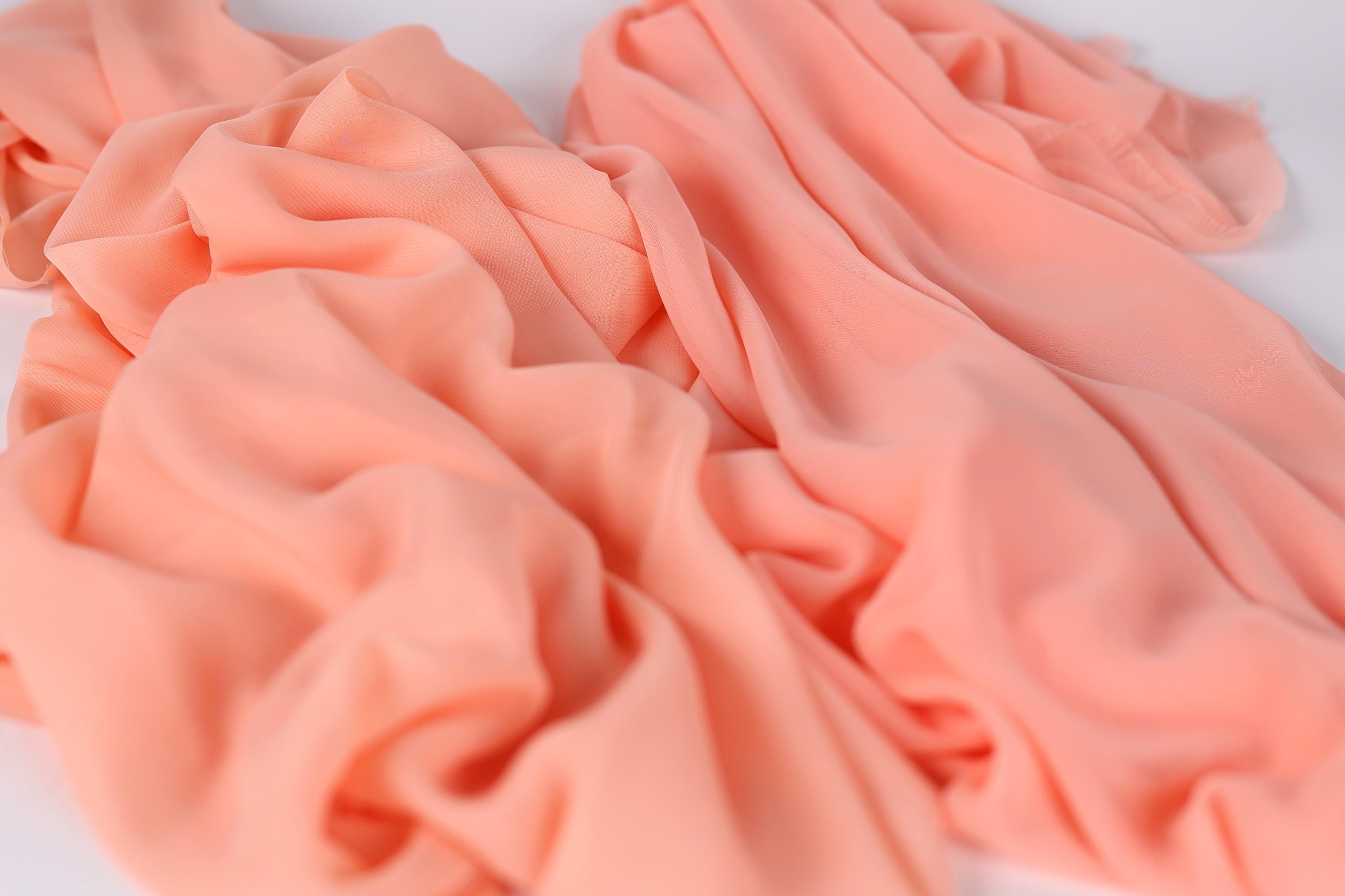 a close-up view of a soft, light pink fabric, possibly chiffon or silk, with a slightly wrinkled texture.
