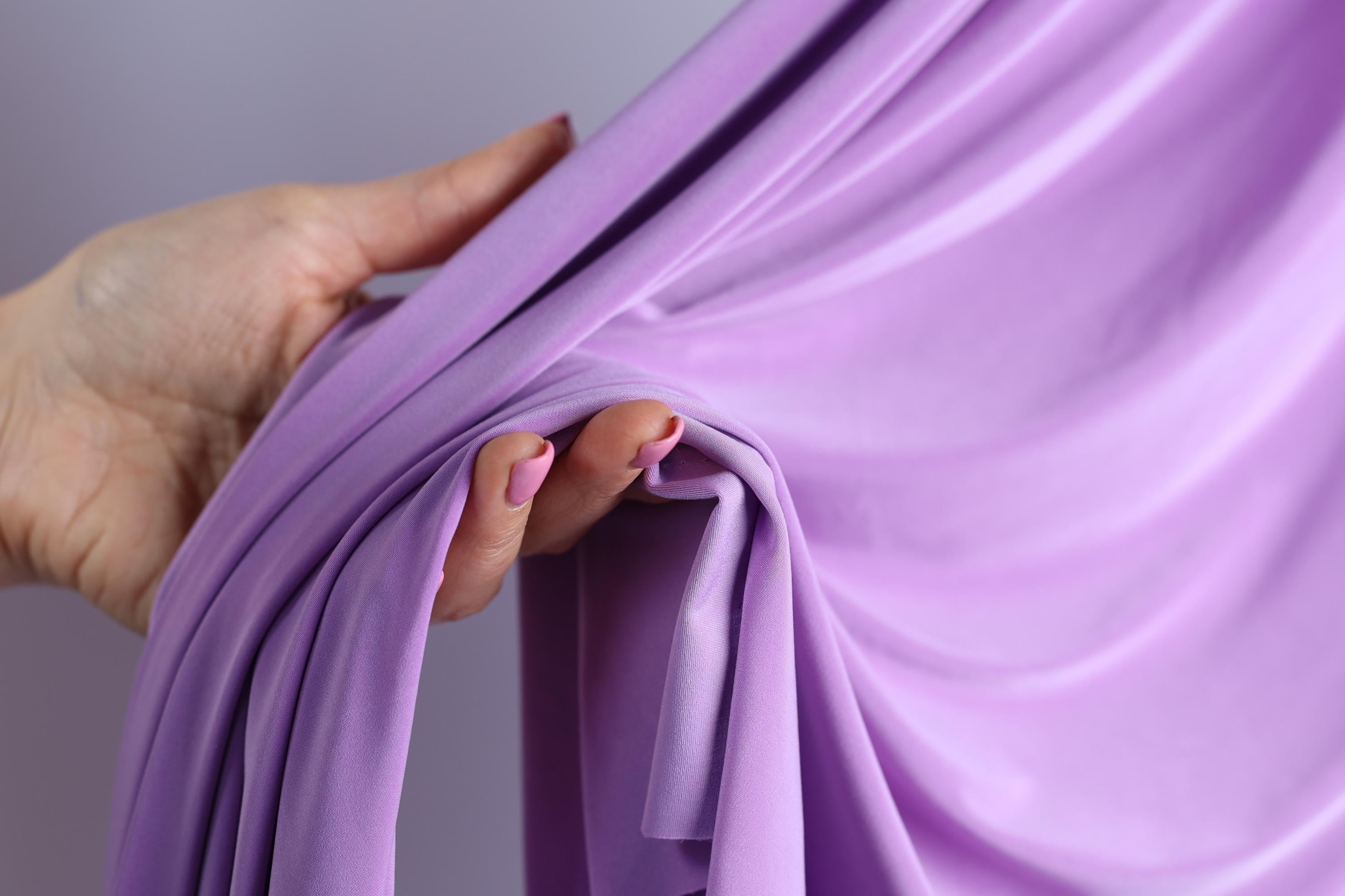 A hand holding a purple fabric, with the fabric partially draped over the hand.