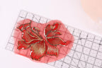 a red and gold embroidered flower design placed on a red measuring mat, with a ruler visible in the background.