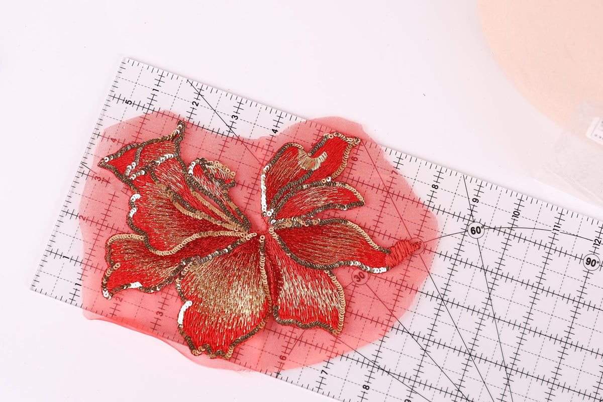 a red and gold embroidered flower design placed on a red measuring mat, with a ruler visible in the background.