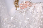 A hand is holding a delicate white lace veil with intricate floral designs.