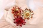 A close-up image of a light pink fabric with three large, ornate flower-shaped embellishments in gold, red, and orange colors.