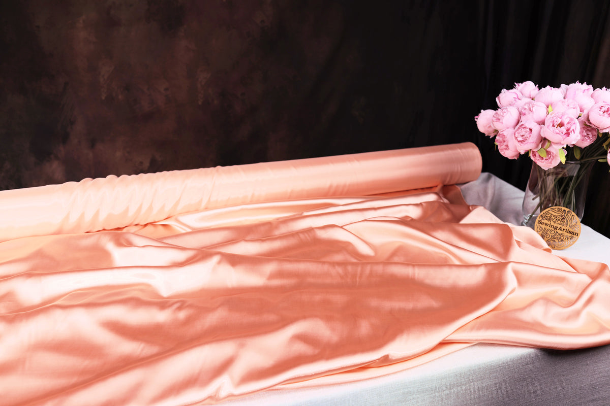 a roll of pink satin fabric and a vase of pink roses on a table.