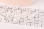 A close-up view of a ruler with a lace pattern on it, placed on a white surface.