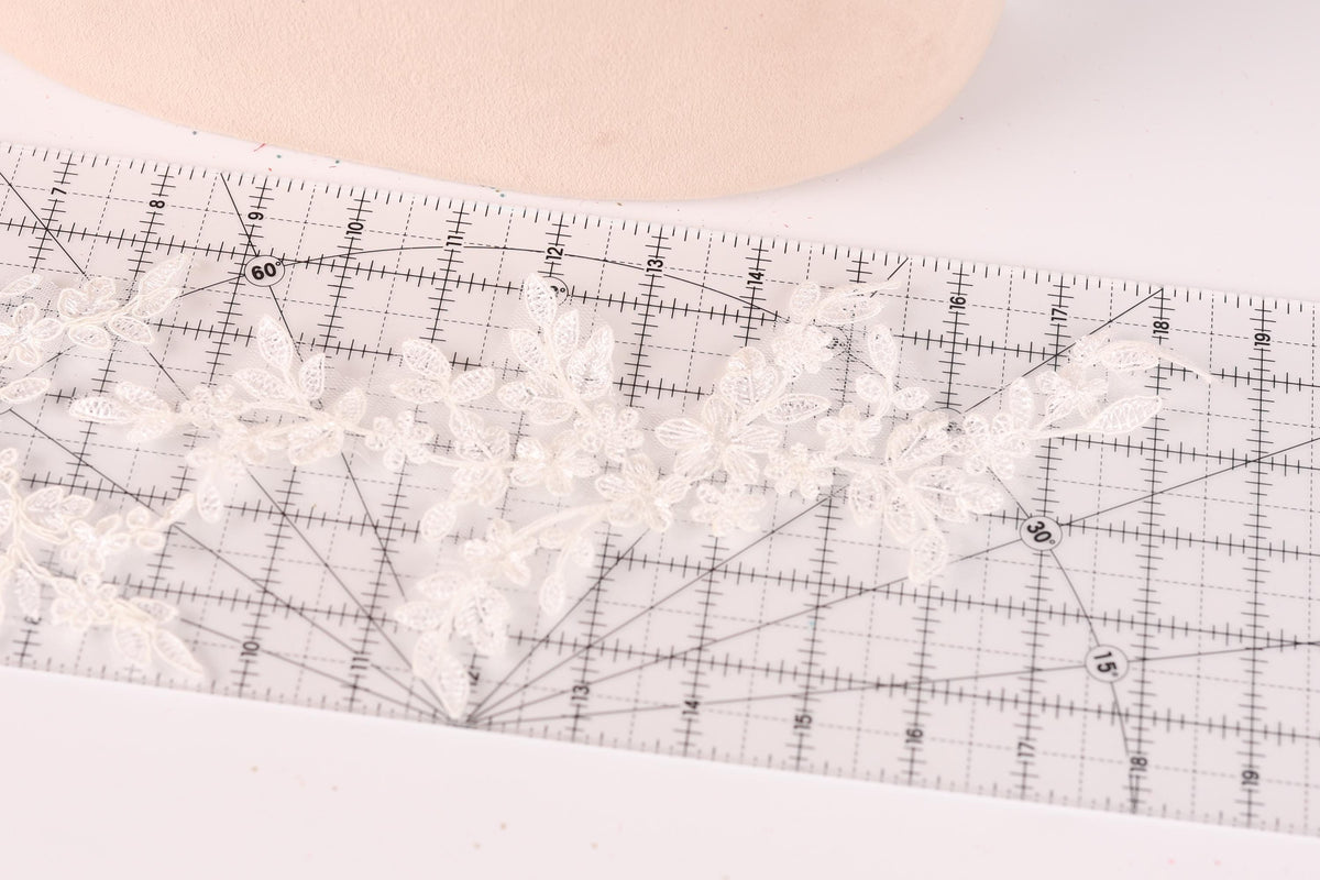 A close-up view of a ruler with a lace pattern on it, placed on a white surface.