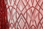 a close-up view of a fabric with a repeating pattern of red and black sequin designs. The pattern consists of various shapes and lines, creating a visually striking and intricate design. The fabric appears to be a light pink color, which contrasts with the red sequins and adds to the overall visual appeal of the image.