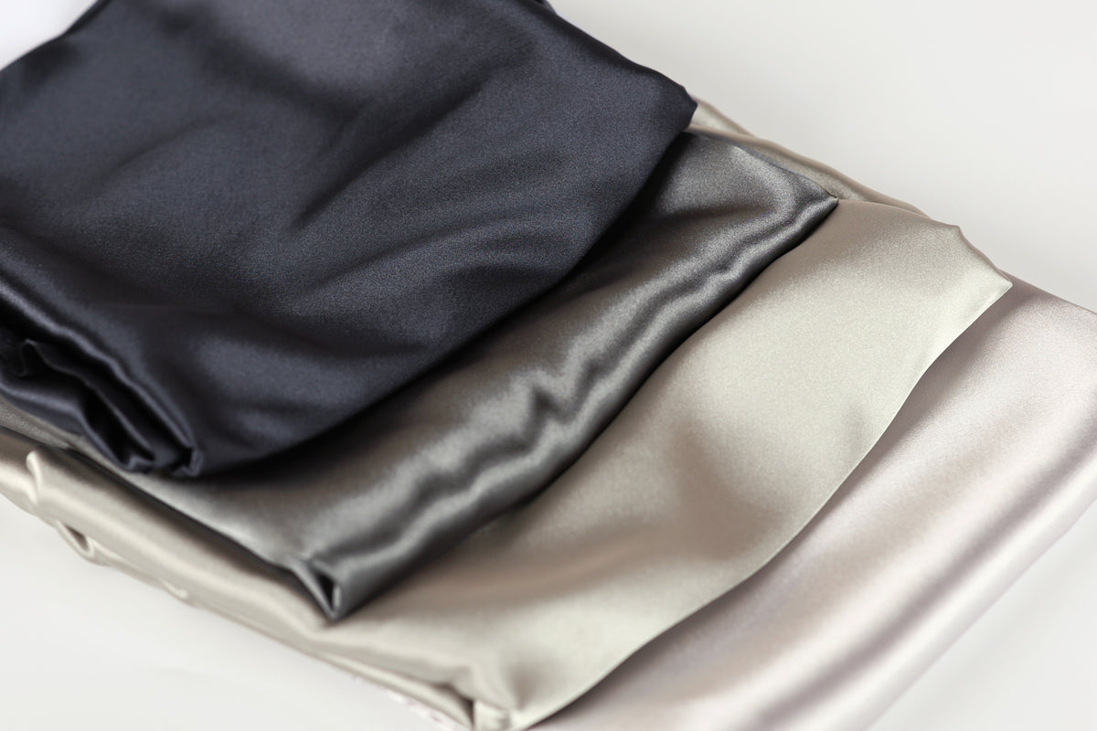 a close-up view of three different colored satin fabrics, including black, gray, and white, arranged in a layered fashion.