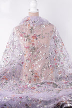 a close-up view of a delicate, intricately embroidered fabric with a floral pattern. The fabric appears to be made of sheer material, allowing the viewer to see the detailed embroidery work. The background is a plain white color, which contrasts with the vibrant colors of the fabric and draws attention to the embroidered design.