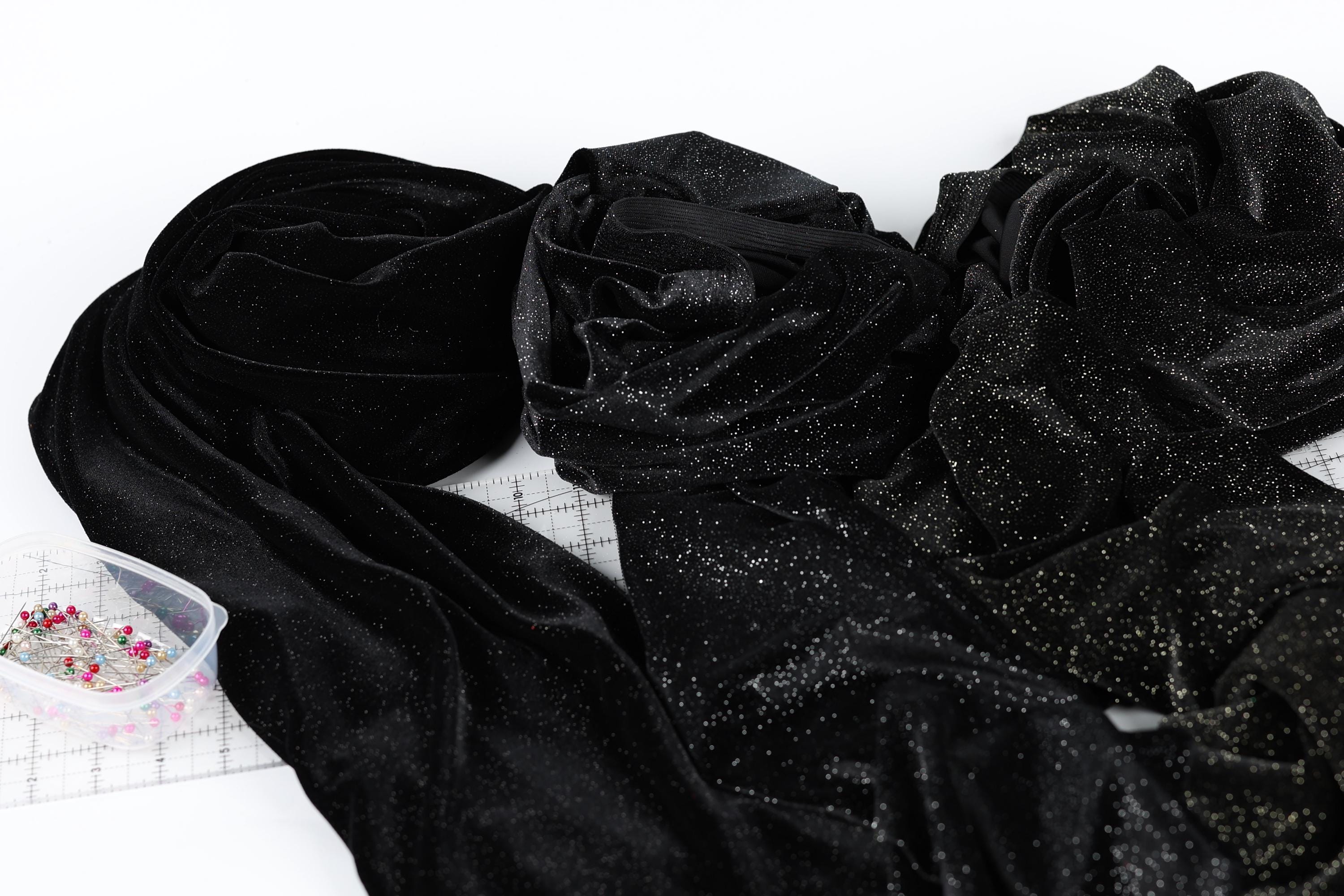 a close-up view of a black fabric with glittery or sparkly elements, possibly a piece of clothing or a decorative material. There is a small container of pins or sewing tools placed next to the fabric.