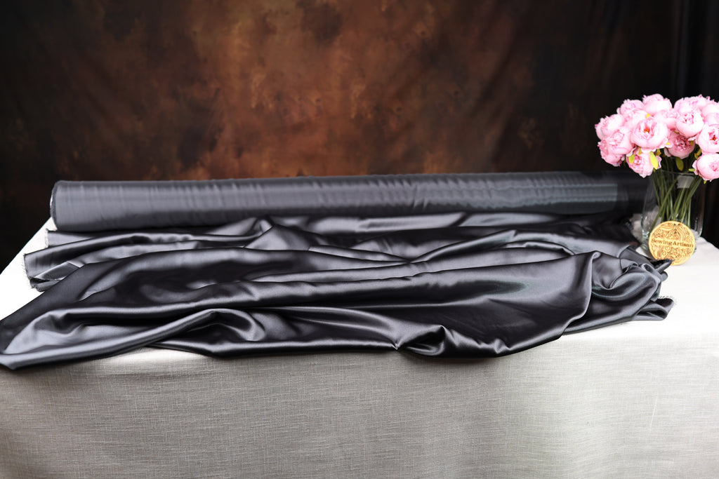 a black satin fabric, a vase of pink flowers, and a dark background.