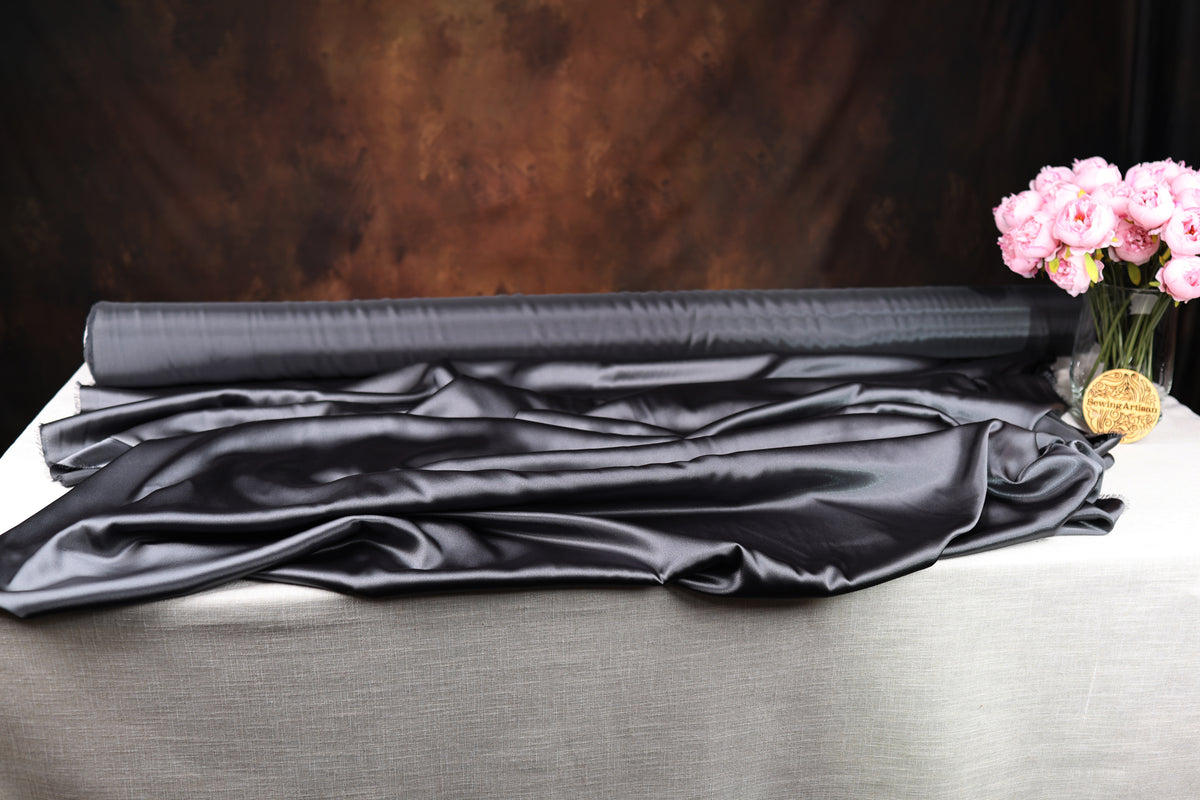 a black satin fabric, a vase of pink flowers, and a dark background.