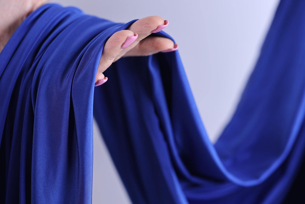 A hand with painted fingernails is holding a blue fabric, with the fabric partially draped over the hand.