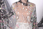 a close-up view of a sheer, floral-patterned fabric, possibly a dress or garment, with a black collar. The fabric appears to be made of sheer material, giving it a delicate and airy appearance.