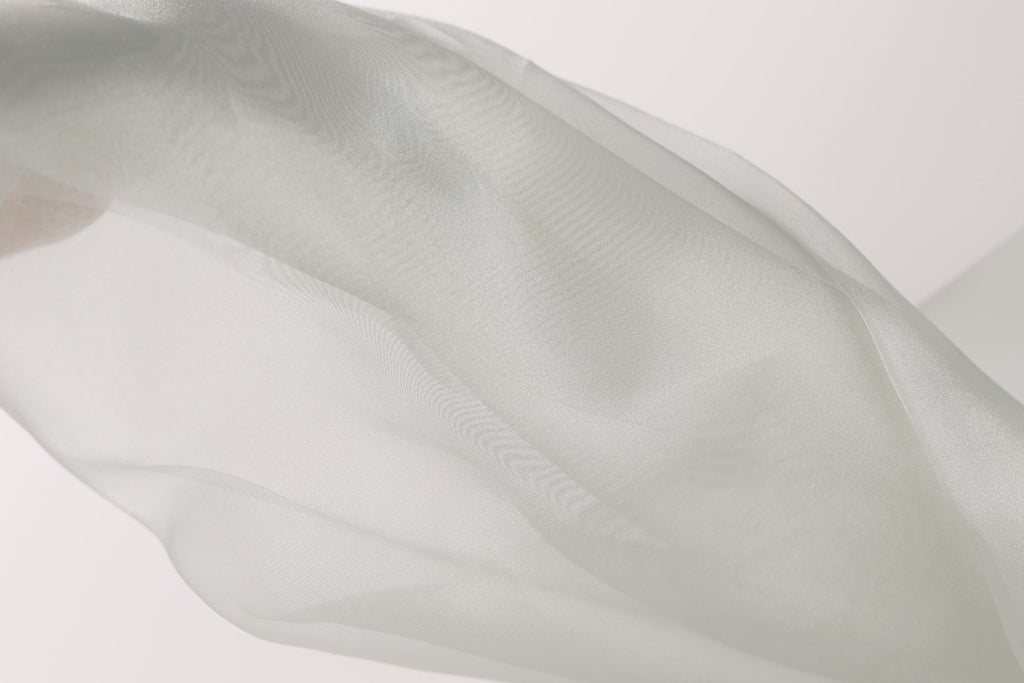 The image is a close-up of a white fabric, possibly a sheer or sheer-like material, with a soft, flowing texture.
