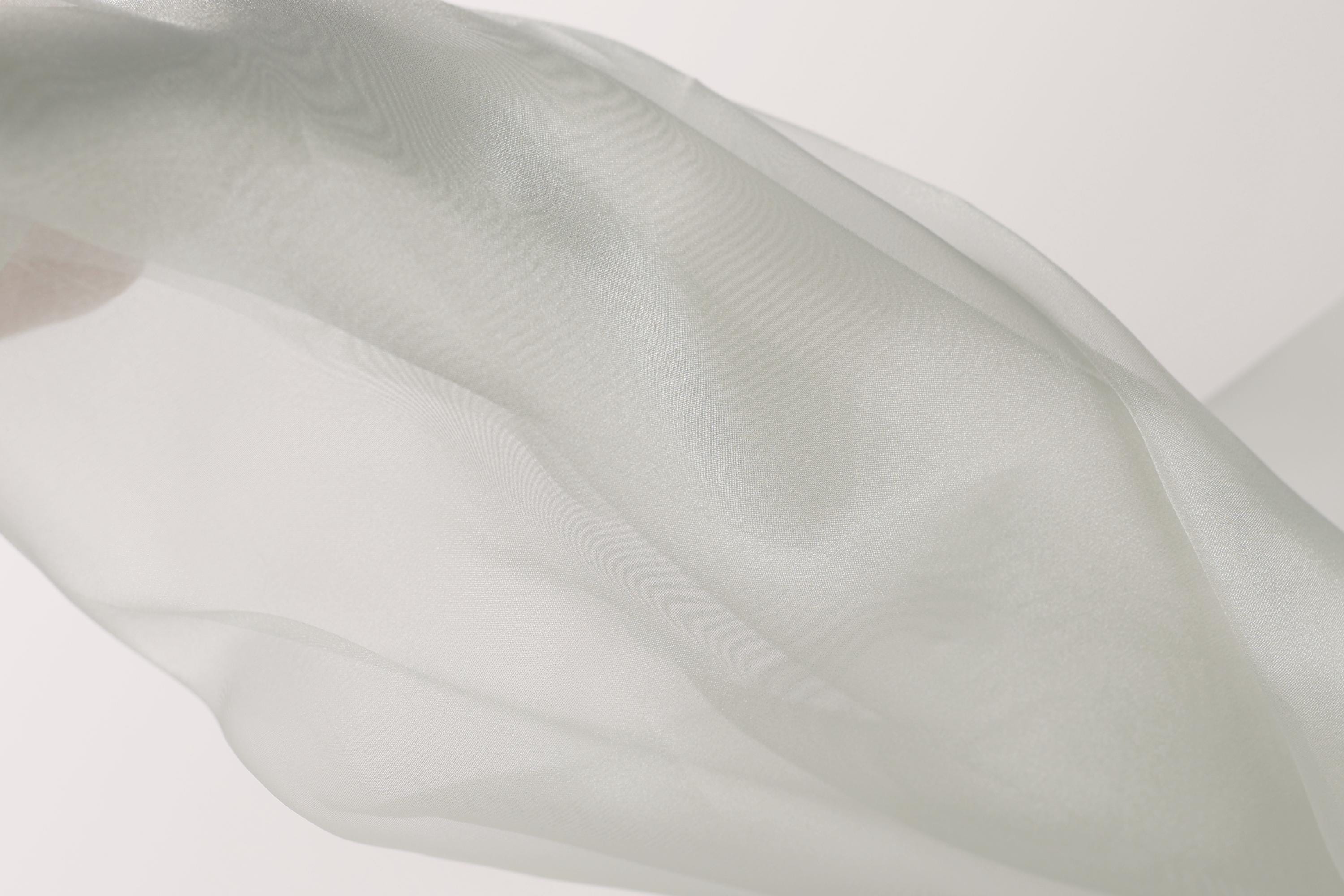 The image is a close-up of a white fabric, possibly a sheer or sheer-like material, with a soft, flowing texture.