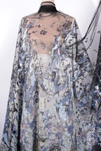 a long, flowing dress with a sheer, sheer-like fabric that has a floral pattern. The dress appears to be made of sequin material, adding a touch of sparkle and glamour to the design.