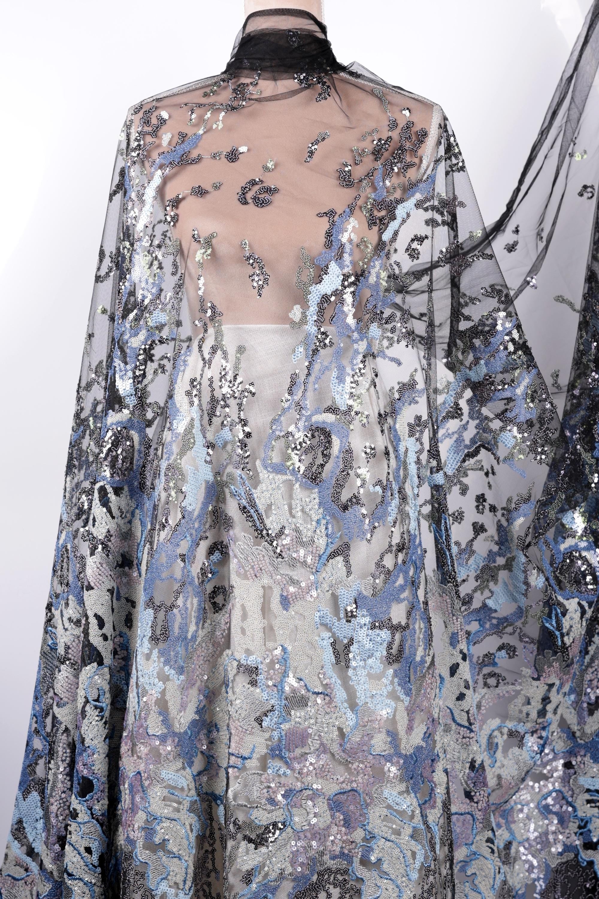 a long, flowing dress with a sheer, sheer-like fabric that has a floral pattern. The dress appears to be made of sequin material, adding a touch of sparkle and glamour to the design.