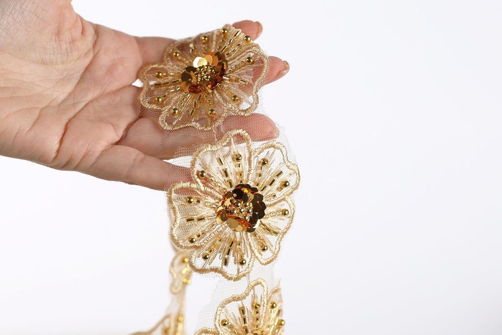 A hand holding a delicate gold and white floral-shaped piece of jewelry, possibly a necklace or bracelet.