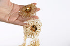 A hand holding a delicate gold and white floral-shaped piece of jewelry, possibly a necklace or bracelet.