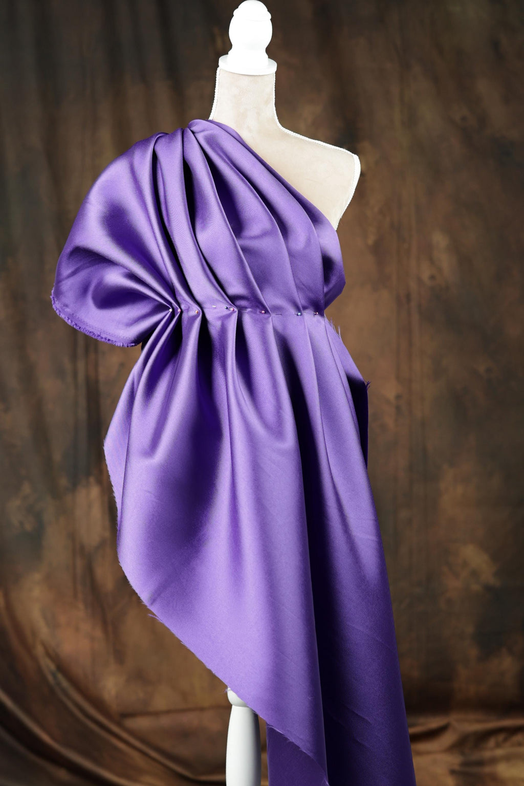A mannequin wearing a purple one-shoulder dress with a flowing, draped design.
