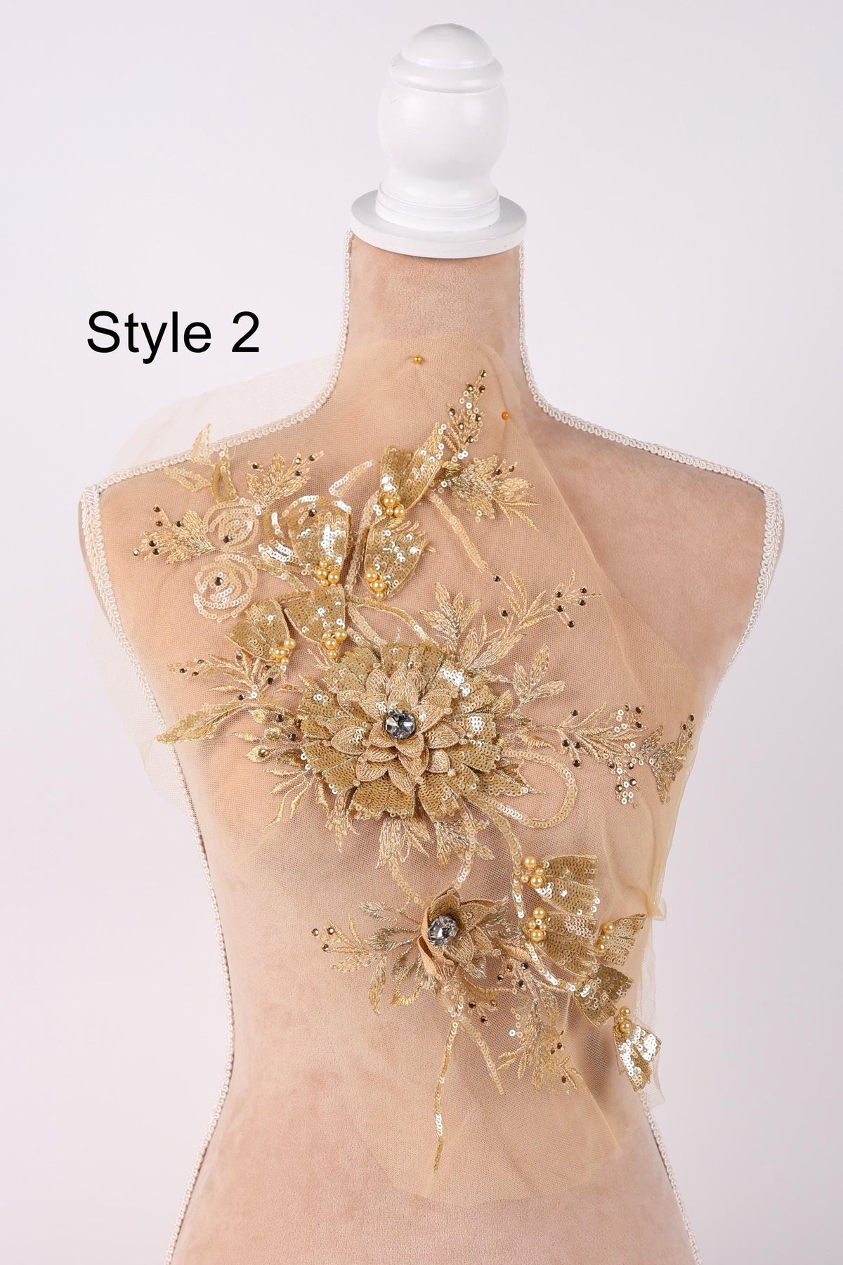 A mannequin with a beige dress and a gold floral embellishment on the shoulder.
