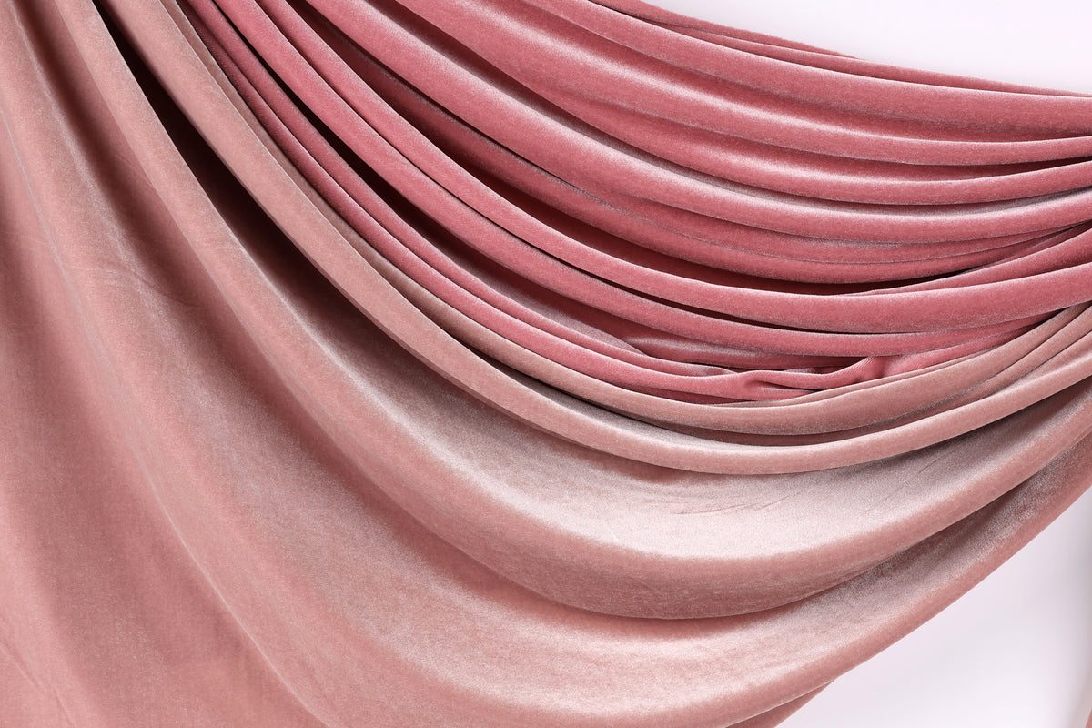 a close-up view of a fabric with a soft, flowing texture in shades of pink and red. The fabric appears to be made of a soft, plush material, possibly velvet or a similar type of material. The fabric is draped or folded in a way that creates a sense of movement and depth, with the colors gradually transitioning from a lighter shade at the top to a darker shade at the bottom.