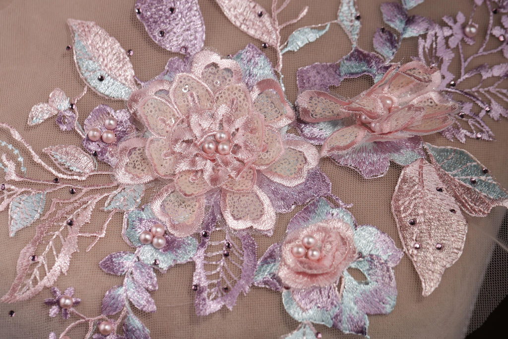 a close-up view of a delicate, intricately embroidered floral design. The design is composed of various pink and purple flowers, leaves, and pearls, all meticulously stitched together to create a visually appealing and detailed piece of textile art.