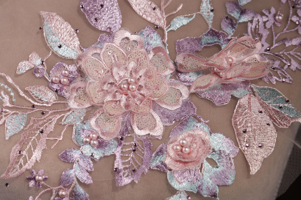 a close-up view of a delicate, intricately embroidered floral design. The design is composed of various pink and purple flowers, leaves, and pearls, all meticulously stitched together to create a visually appealing and detailed piece of textile art.