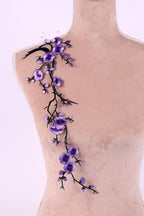 a mannequin with a delicate floral embroidery on its shoulder. The embroidery is composed of purple flowers and branches, creating a beautiful and intricate design.