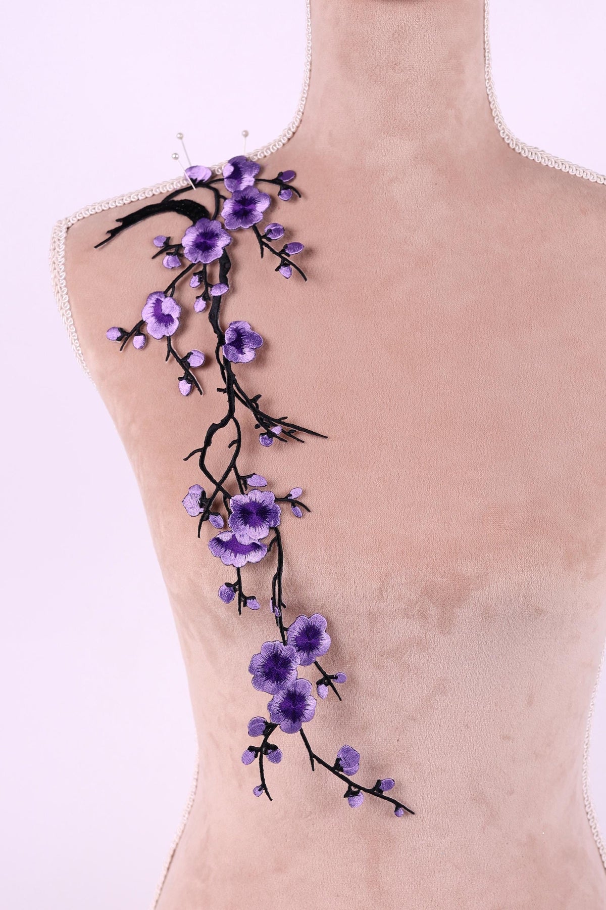 a mannequin with a delicate floral embroidery on its shoulder. The embroidery is composed of purple flowers and branches, creating a beautiful and intricate design.