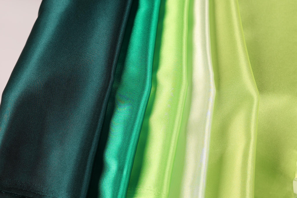A close-up image of a collection of fabric swatches in various shades of green, including dark green, lime green, and mint green.