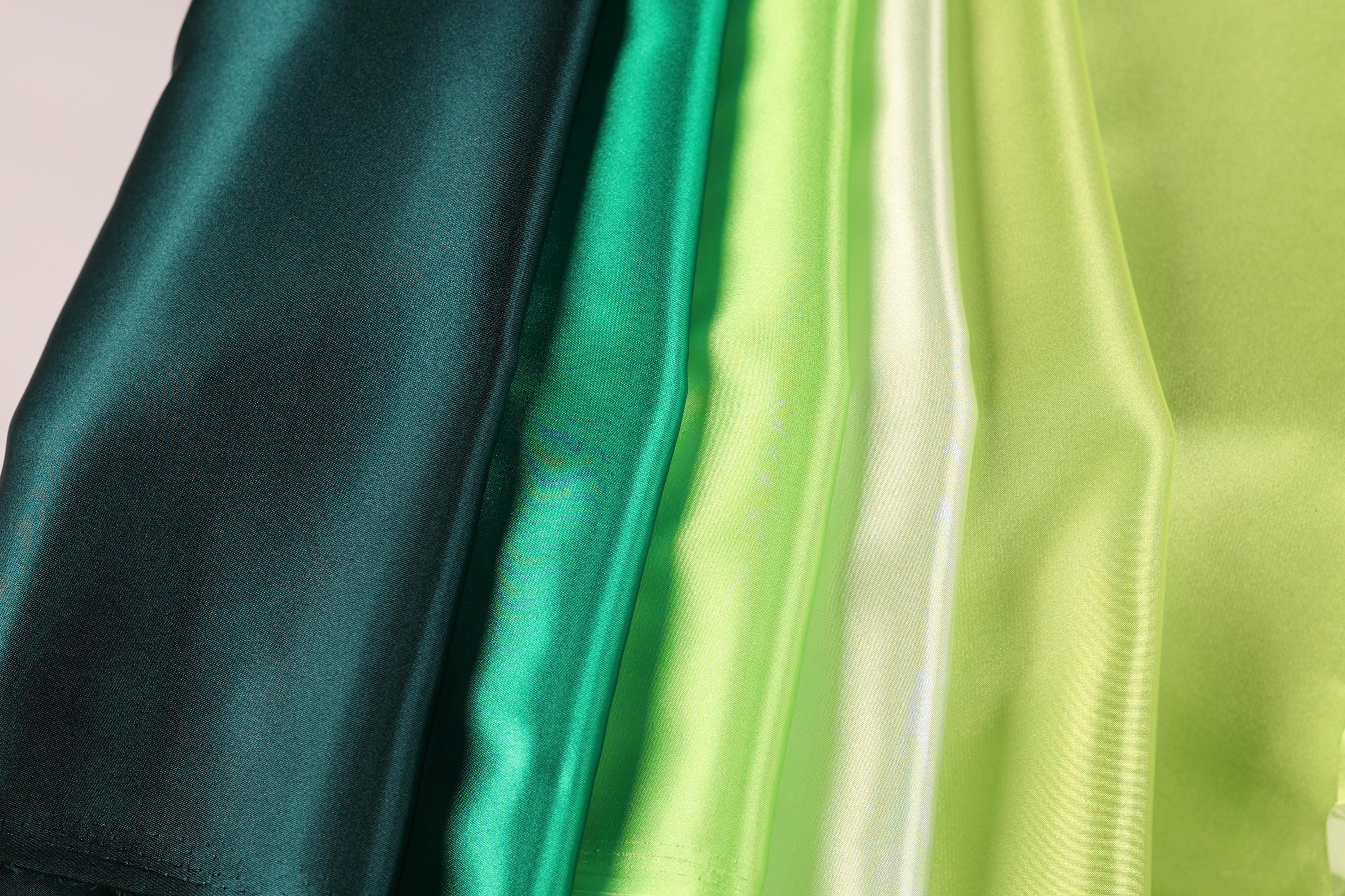 A close-up image of a collection of fabric swatches in various shades of green, including dark green, lime green, and mint green.