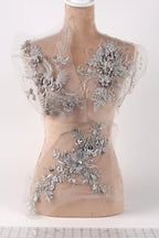a mannequin with a beige body and a white head, adorned with intricate silver floral and leaf designs. The mannequin is displayed on a white surface, and the background is plain white.