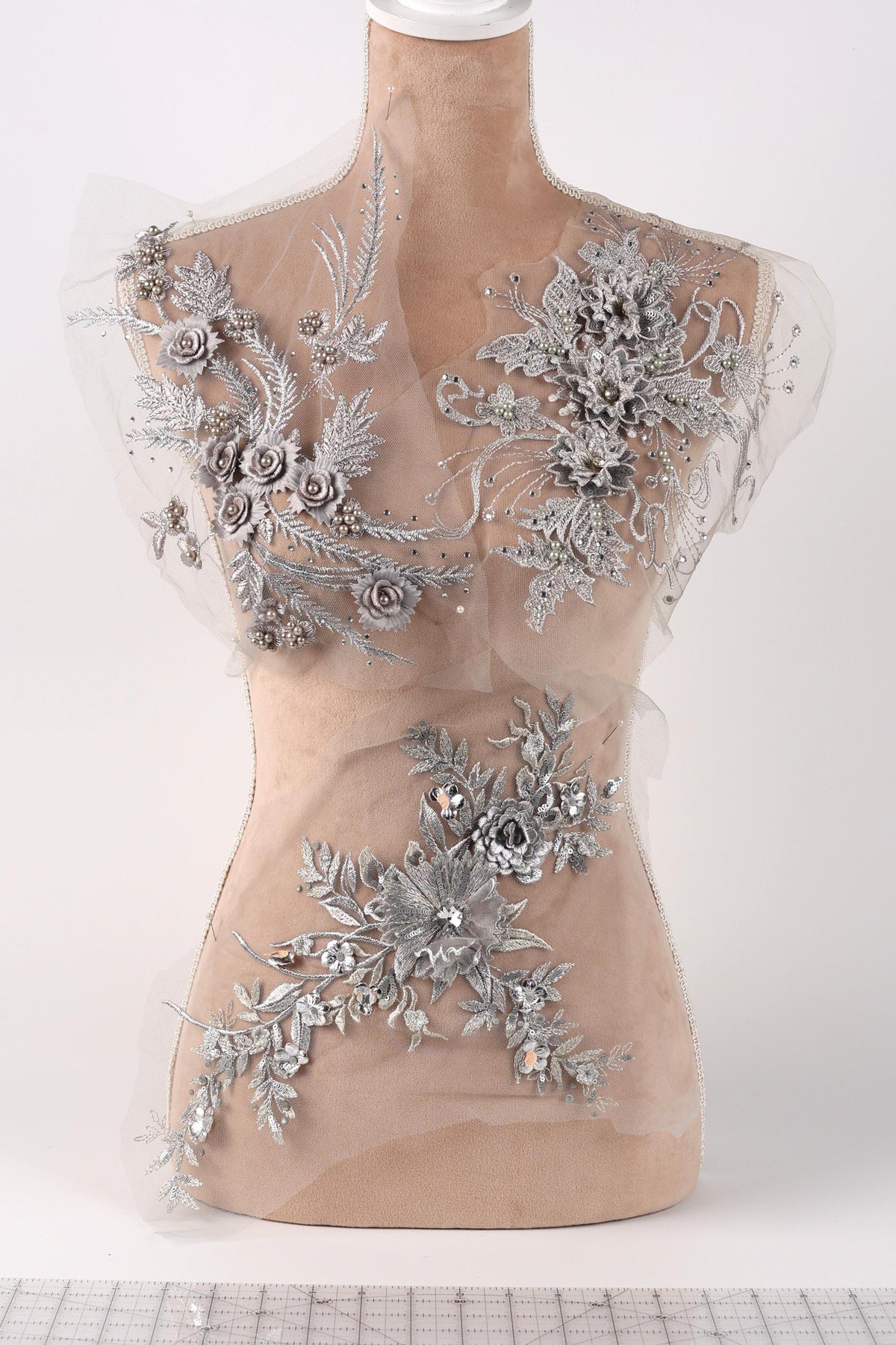 a mannequin with a beige body and a white head, adorned with intricate silver floral and leaf designs. The mannequin is displayed on a white surface, and the background is plain white.