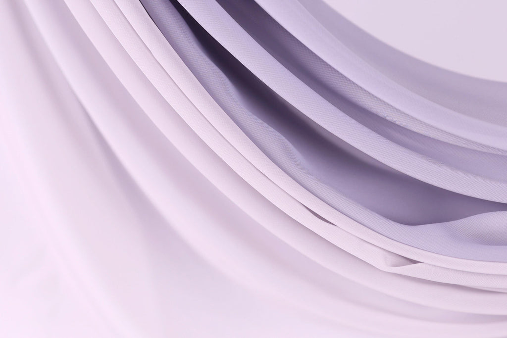 a close-up view of a soft, flowing fabric with a gradient of purple and white colors. The fabric appears to be made of a sheer material, giving it a delicate and elegant appearance.