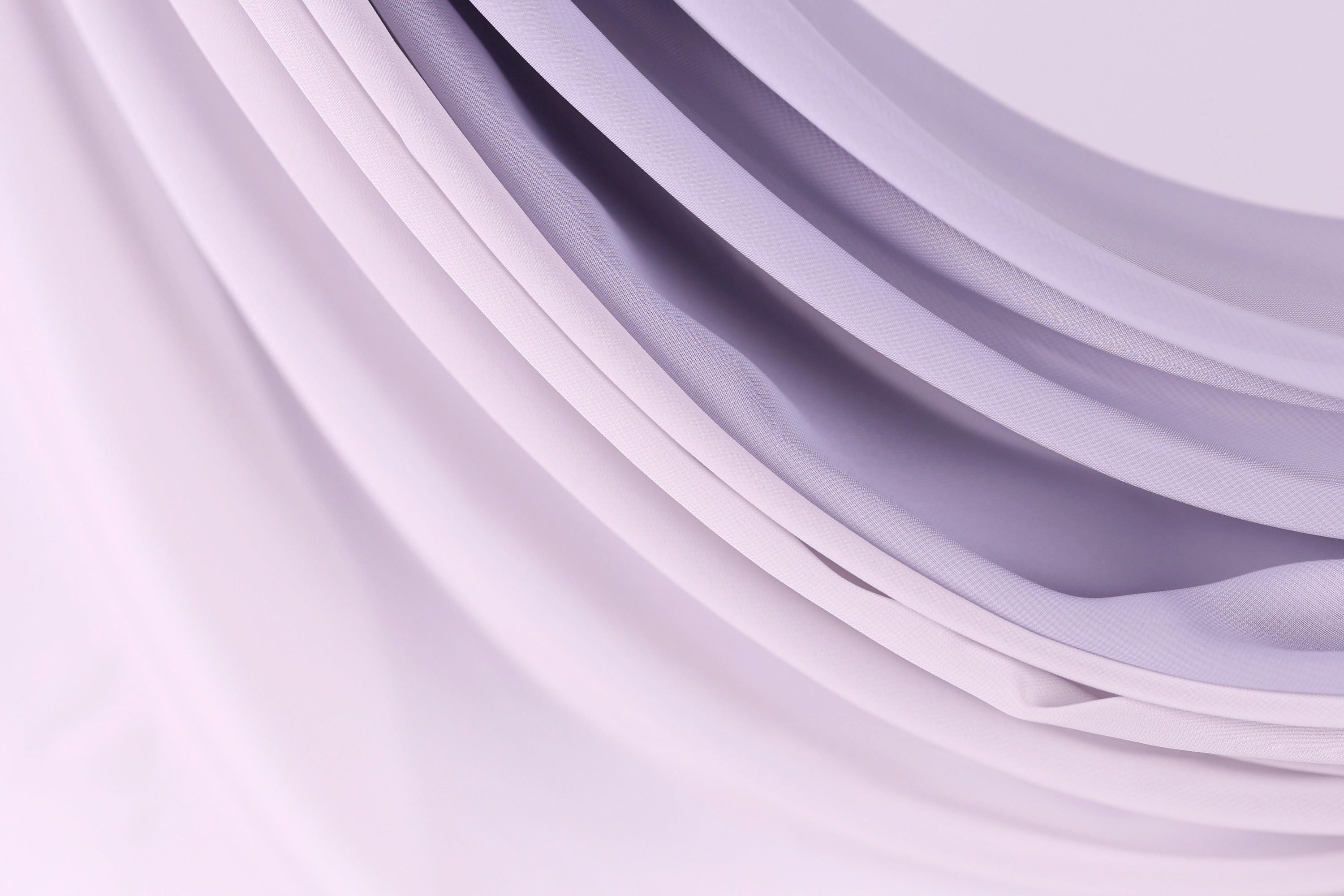 a close-up view of a soft, flowing fabric with a gradient of purple and white colors. The fabric appears to be made of a sheer material, giving it a delicate and elegant appearance.