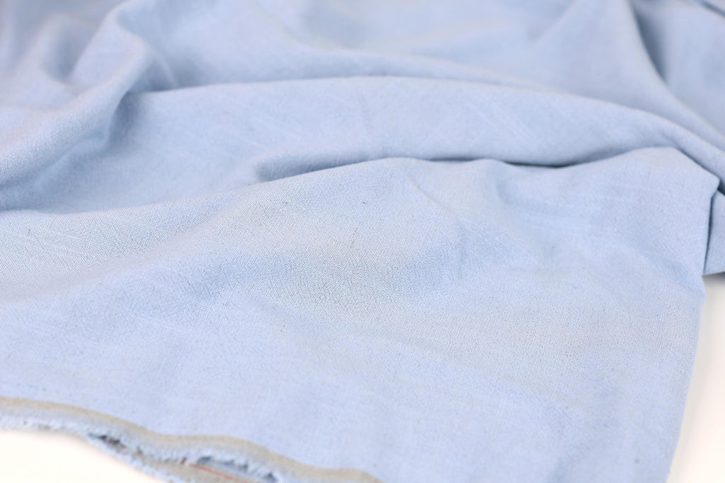 A close-up view of a light blue fabric, possibly denim, with visible wrinkles and folds.