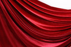 a close-up view of a red velvet fabric, with its smooth and shiny texture visible. The fabric appears to be draped or flowing, creating a sense of depth and movement. The color of the fabric is rich and vibrant, with a deep red hue that contrasts with the white background. The fabric's texture is smooth and shiny, adding to its visual appeal.