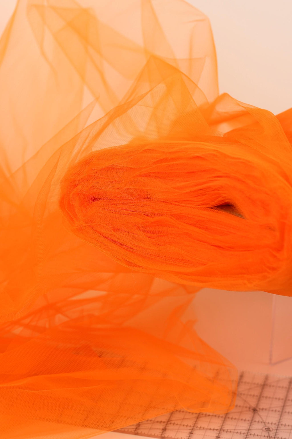a close-up view of a roll of orange tulle fabric, with its vibrant color and soft texture clearly visible.