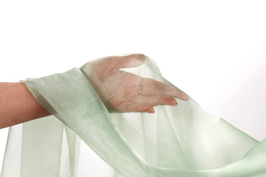 A hand is holding a green fabric, possibly a sheer or sheer-like material, against a white background.