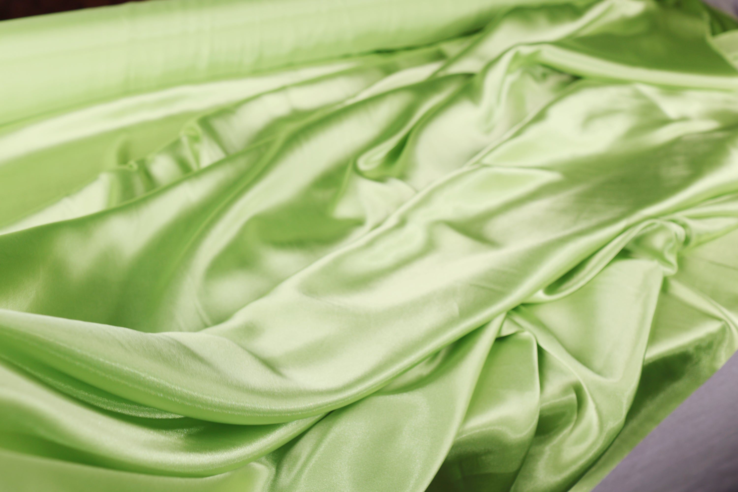 a close-up view of a green satin fabric, with its smooth and shiny texture visible.