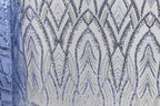 a close-up view of a fabric with a repeating pattern of blue and silver sequins. The pattern consists of a series of arched shapes and lines, creating a visually striking and intricate design. The fabric appears to be a piece of clothing or textile, with the sequins adding a touch of sparkle and elegance to the overall appearance.