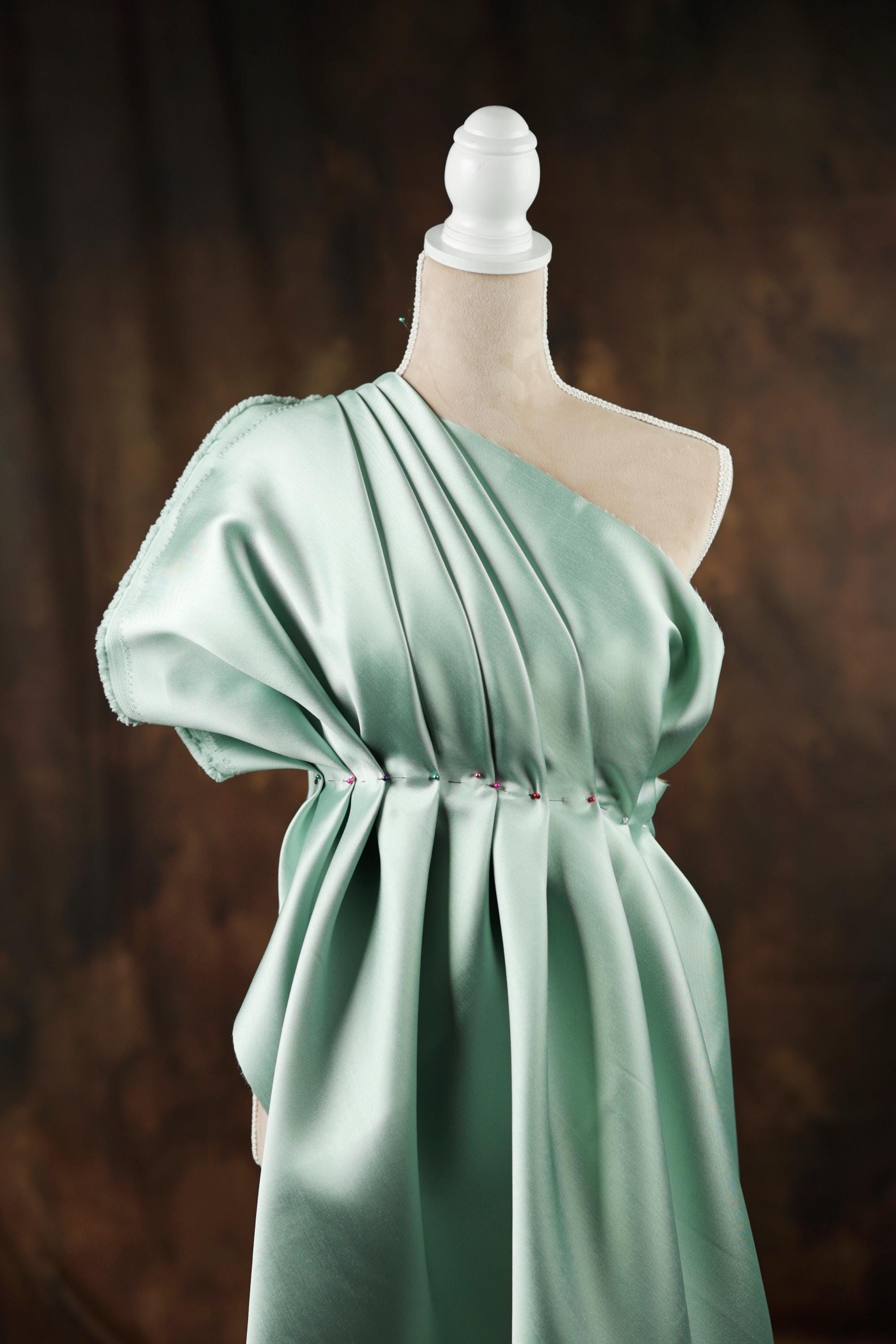 A mannequin wearing a green one-shoulder dress with a pleated design.