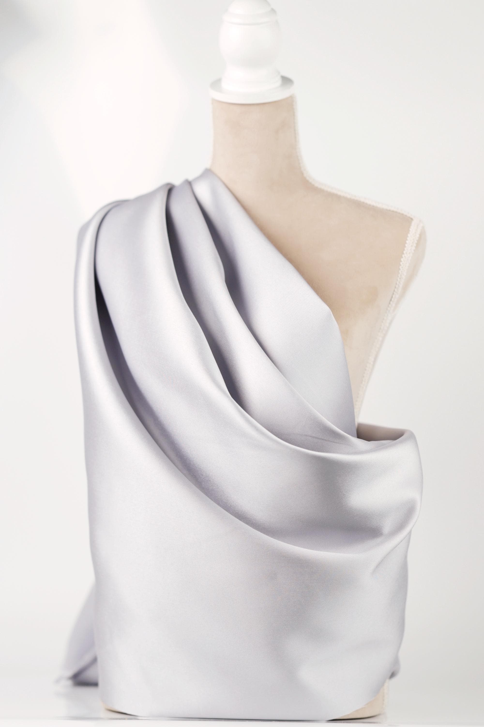 A mannequin wearing a gray satin fabric draped over its shoulder.