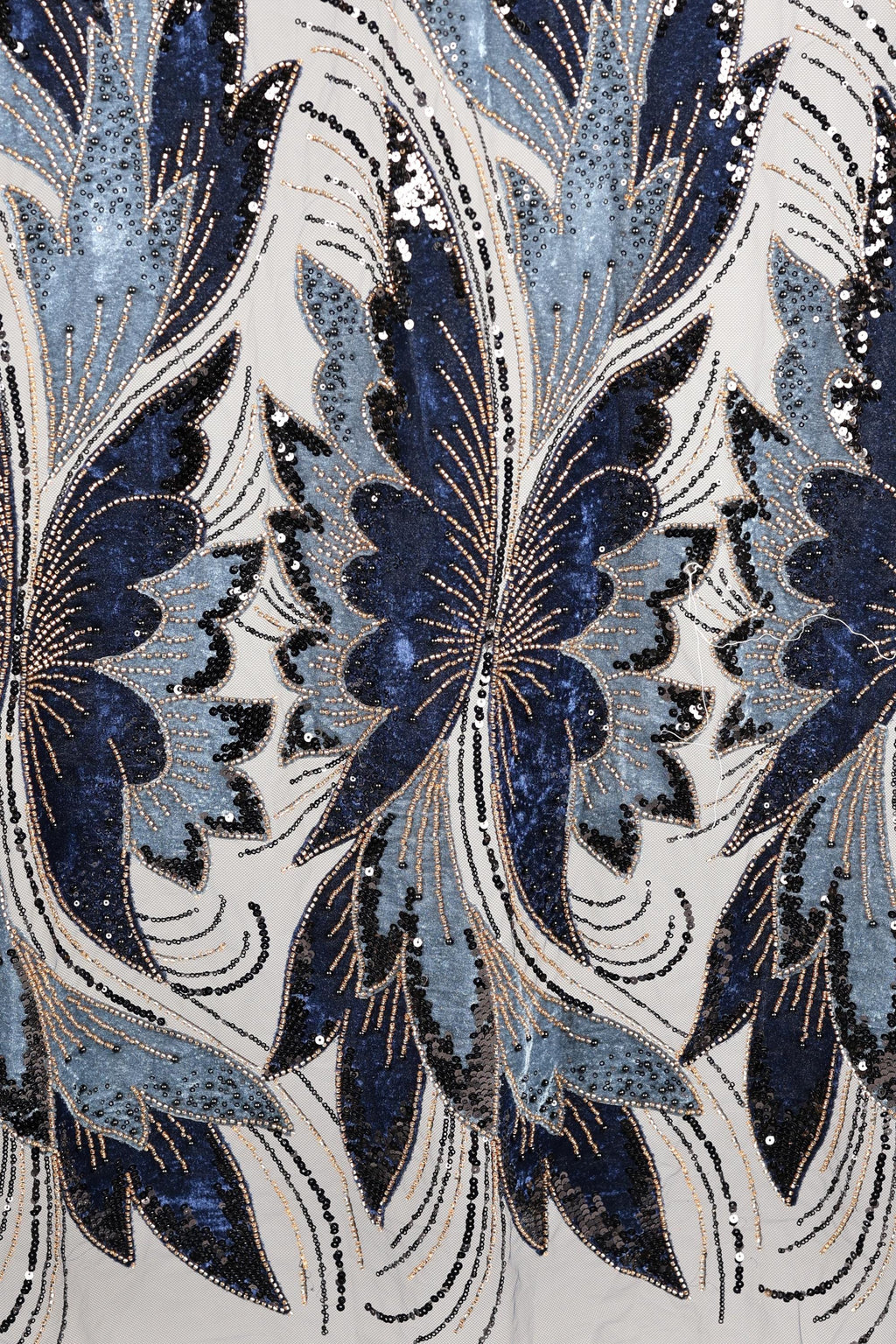 a close-up view of a fabric with a repeating pattern of blue and white butterfly-like shapes, adorned with sequins and beads. The pattern is intricate and detailed, showcasing the craftsmanship and artistry involved in creating the fabric.