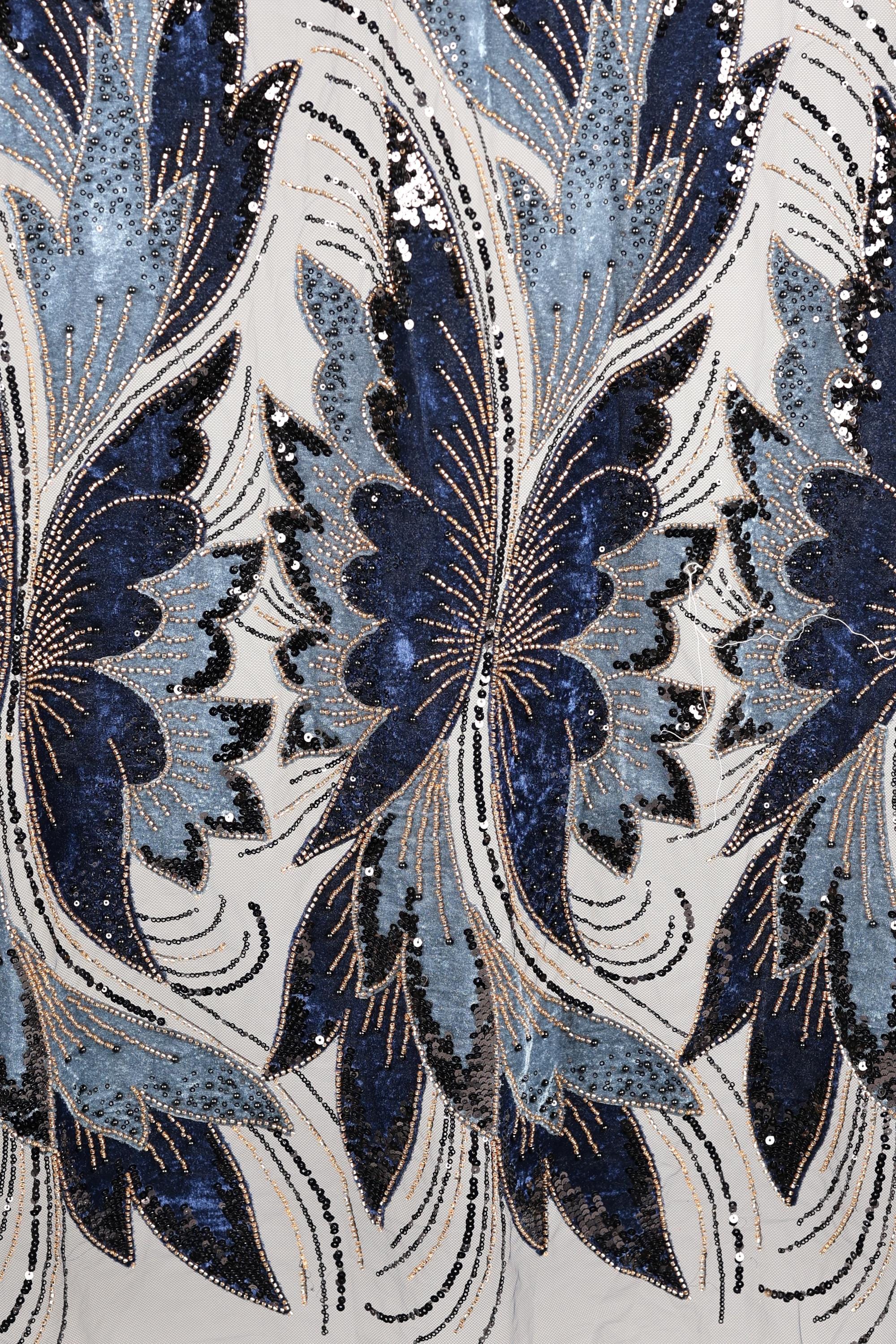 a close-up view of a fabric with a repeating pattern of blue and white butterfly-like shapes, adorned with sequins and beads. The pattern is intricate and detailed, showcasing the craftsmanship and artistry involved in creating the fabric.
