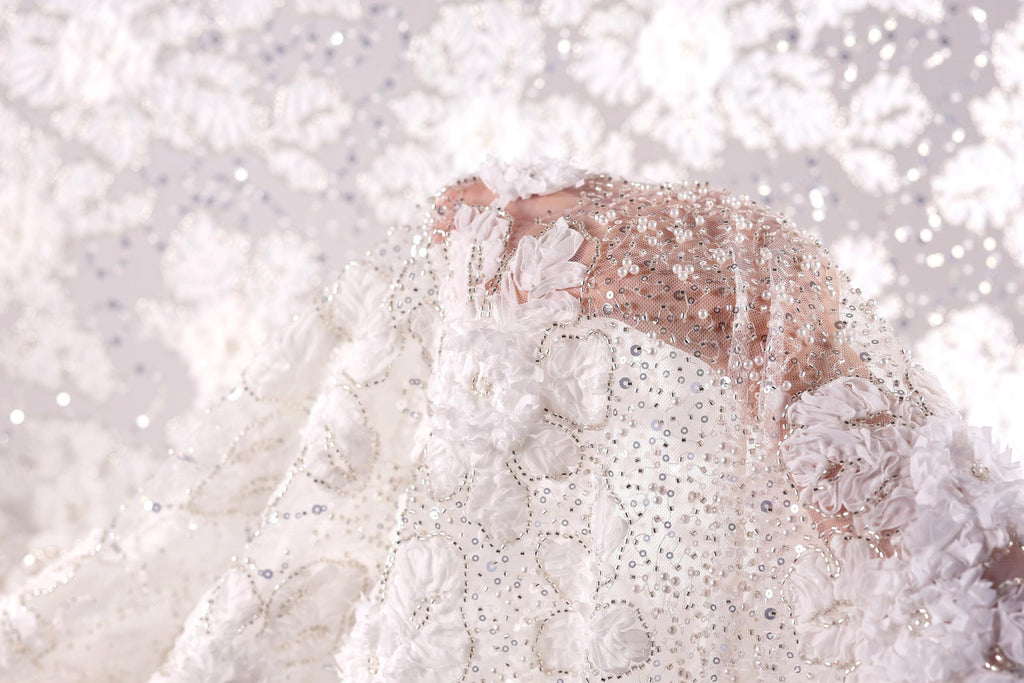 A close-up view of a delicate, white lace dress with intricate beading and floral embellishments.