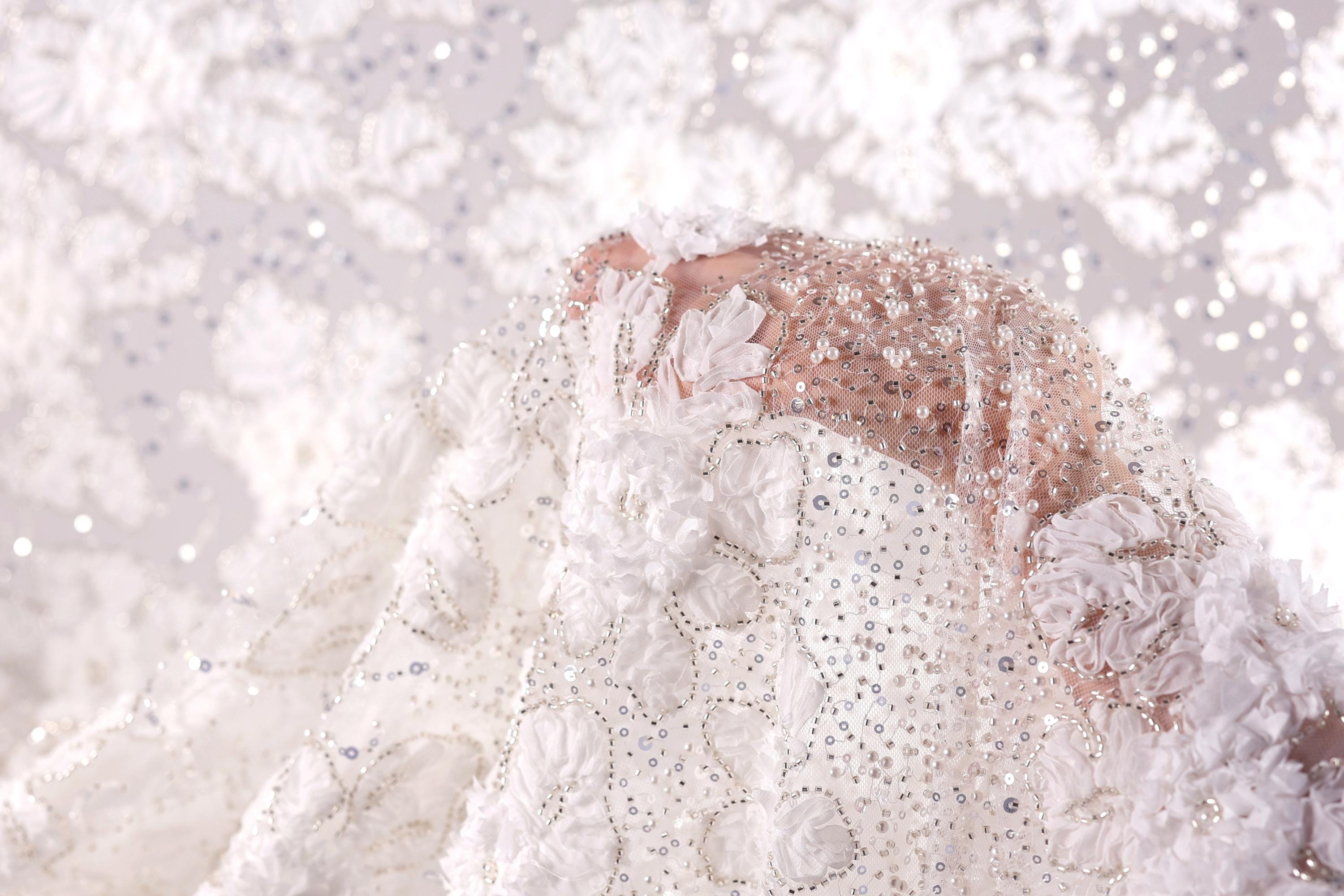A close-up view of a delicate, white lace dress with intricate beading and floral embellishments.